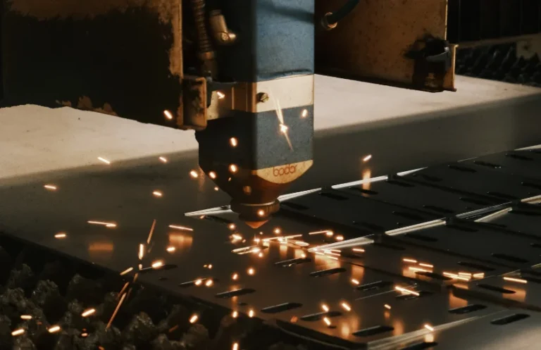 Cabezal de un equipo láser industrial realizando un grabado detallado y de alta precisión sobre una placa de aluminio anodizado negro, despidiendo chispas brillantes controladas.