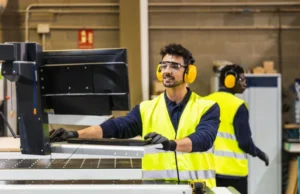 Ingeniero de soporte técnico local capacitando a un operario en el panel de control de una máquina CNC en un taller industrial.